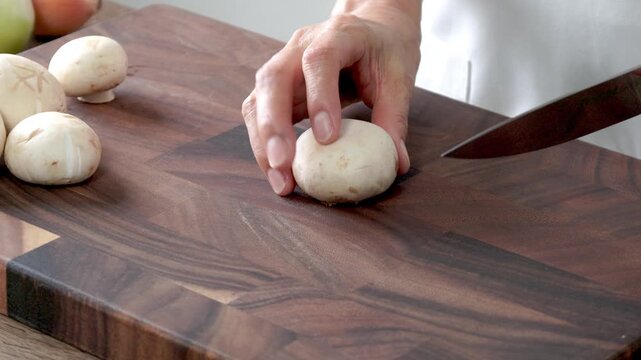 A woman prepares food in the kitchen at home. Slices mushrooms with a knife on a cutting board