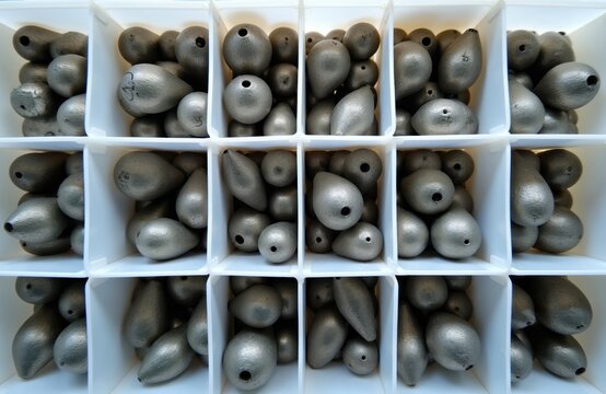 Top view of white plastic container with various metal lead fishing sinkers inside. Many grey oval weights for angling lines sorted by size. Pro equipment for sport hobbyists to catch fish in river