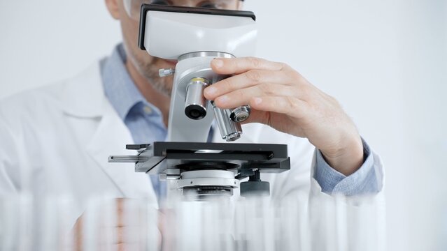 Scientist looking through a microscope in a bright laboratory, performing medical research and scientific discovery, exploring microbiology and biochemistry for new solutions