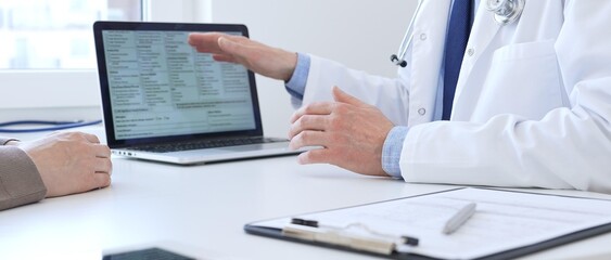 Fototapeta na wymiar Close-up of a doctor reviewing digital test results with patient, discussing health findings on laptop screen during clinical consultation. Medicine and health care concept