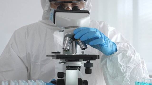 Medical virologist in protective hazmat gear examining viral samples under a microscope while conducting research in a sterile laboratory environment