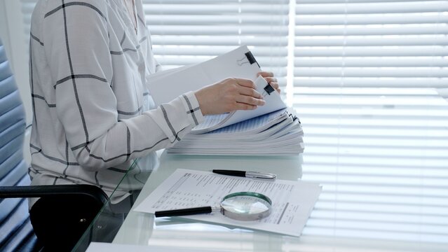 Professional woman categorizing important business documents and financial statements on an office desk. Managing a stack of files during a detailed audit
