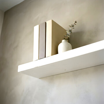 Minimalist decorative shelf display featuring neutral toned books and a small ceramic vase with dried stem
