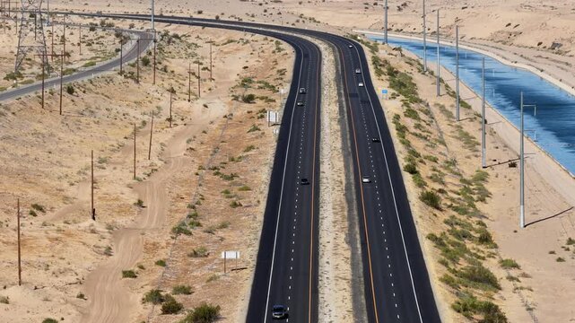 Highway running parallel to a long water canal through a dry sandy landscape, high-angle aerial view