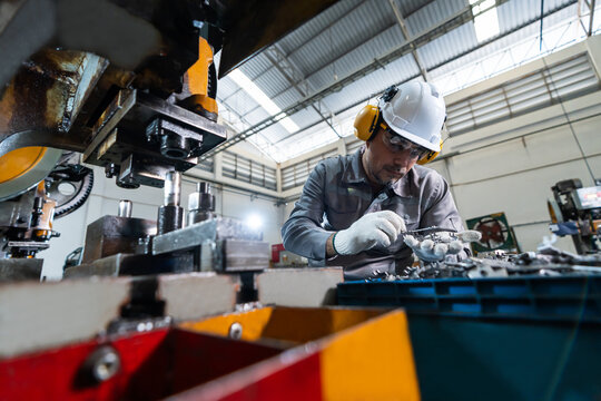 A white male factory worker in workwear,hard hat,protective glasses and earmuffs inspecting automotive metal components in sheet metal stamping manufacturing plant