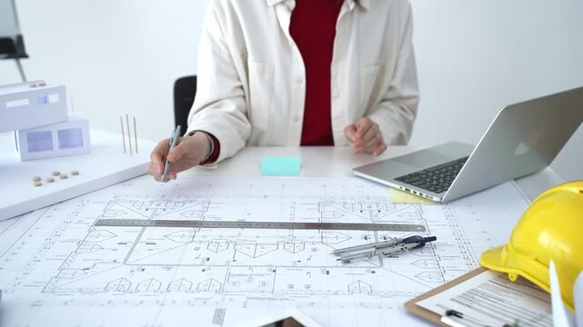 Architect working on new residential project using laptop, reviewing blueprints and drafting floor plans for modern building design with a 3d model on office desk