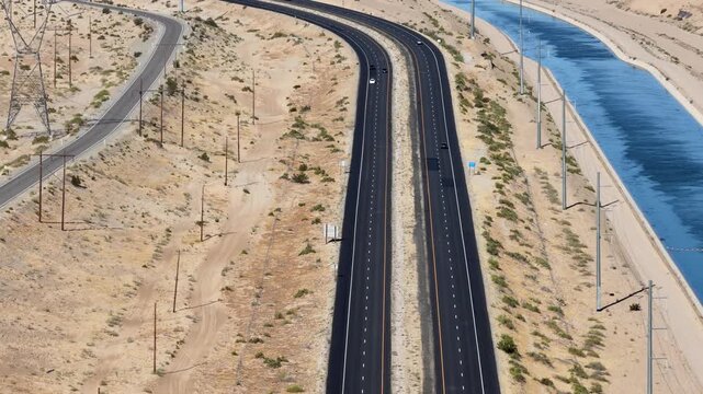 Highway running parallel to a long water canal through a dry sandy landscape, high-angle aerial view
