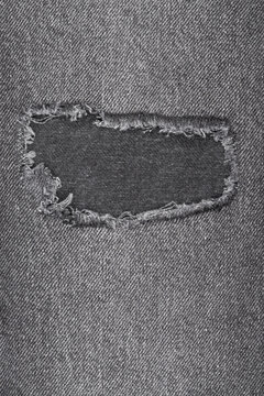 Closeup of old, worn grey denim. Ripped rectangular hole with frayed edges shows fabric texture. Background for design, fashion or concepts of durability and decay