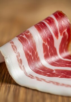 Close-up macro view of a thin pancetta slice showing intricate white fat marbling and deep pink cured meat textures on a wooden surface, details, cured, butcher