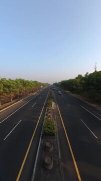 GRESIK, INDONESIA - JULY 19, 2026: High angle vertical timelapse of highway traffic with vehicles and green trees during a bright morning.