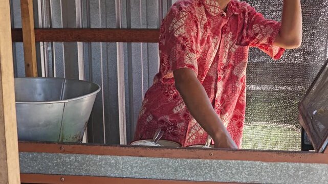 Man wearing traditional batik shirt preparing local street food at a rustic food stall in Indonesia