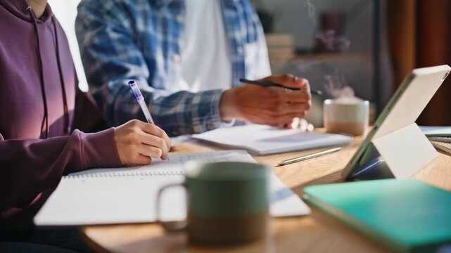 Multiethnic couple studying together home. Closeup hands writing notes tablet
