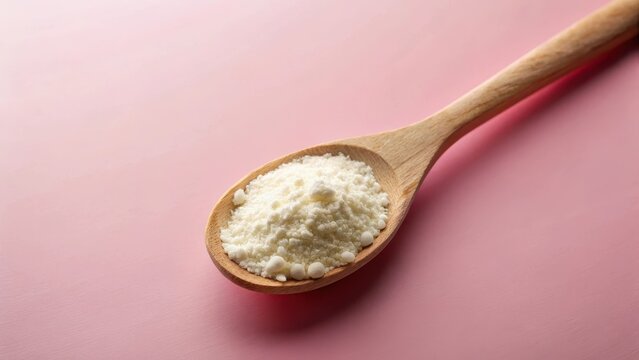 A delicate dusting of colostrum skim milk powder coated a vintage wooden spoon on a soft pink background