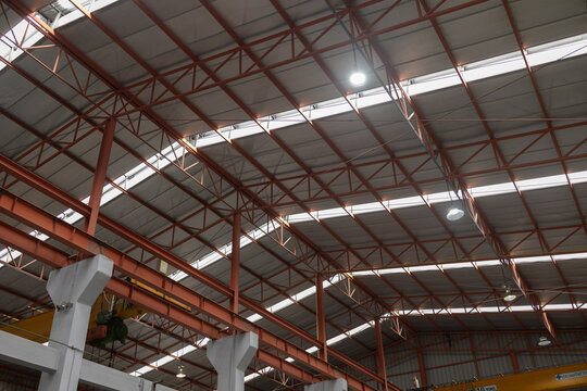 Vast impressive interior roof structure of an industrial factory concept featuring sturdy steel beam frame and corrugated metal sheet roofing with bright skylight illumination