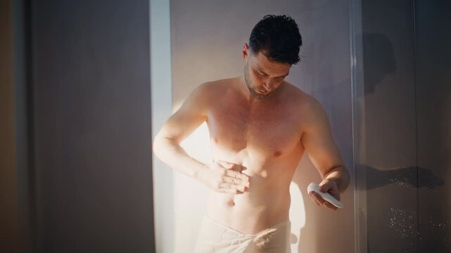 Man applying body lotion after shower. Shirtless guy skin moisturizing routine