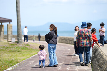 Fototapeta premium Mother walks with child along seaside path. Family strolls near water's edge under clear sky. People appear calm, enjoying peaceful coastal walk. Image suits family vacation, leisure