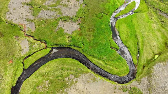 Overhead aerial of meandering river winding through bright green floodplain, shallow reflective channel, gravel bars, mossy banks, and exposed bed forming broad natural curves