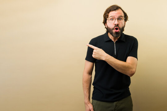 Surprised man pointing to the side, open mouth showing reaction. Ideal for unexpected news, advertising, or promotional content