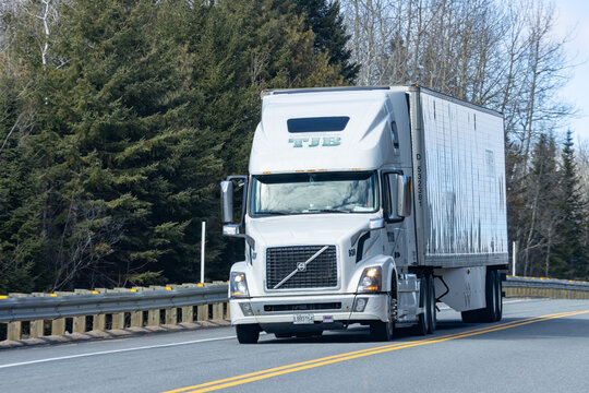 Quebec, Canada, 24 April 2026 : A white Volvo TJB Transport semi truck drives on a highway next to a forest.