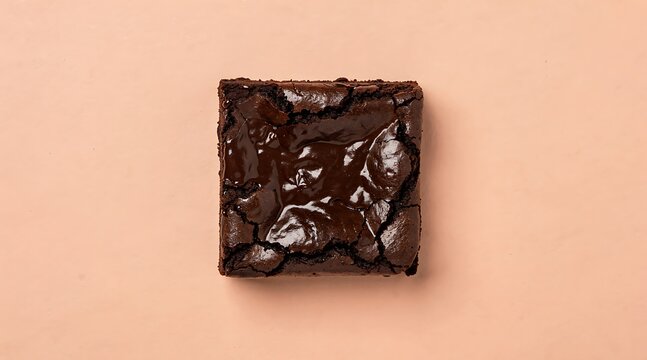 A single, rich, dark chocolate brownie with a cracked, glossy top, presented on a plain peach background.