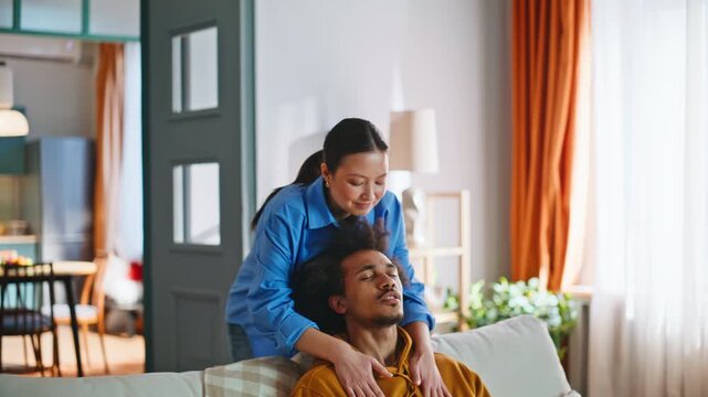 Asian girlfriend massaging boyfriend shoulders. Multiracial couple at home.