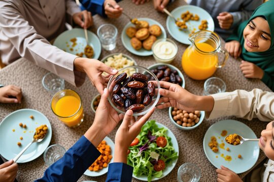Muslim family breaks fast together at home table for Ramadan iftar meal. Children and adults share healthy food dates and juice. Festive gathering celebrates Islamic holy month with joy.