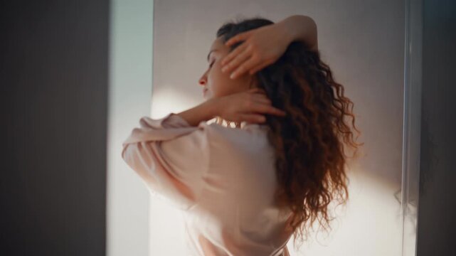 Sensual woman removing silk robe home. Curly hair lady back view sunlight.