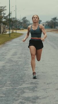 Front tracking shot of female runner passing a tree lined road