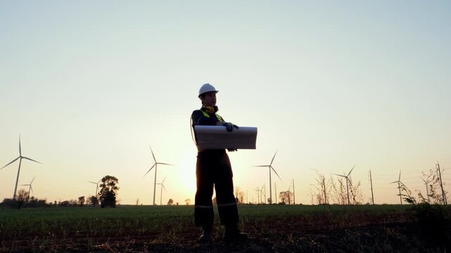 Professional worker examines document outdoors during vibrant sunset illuminating multiple wind turbines creating symbol of renewable energy innovation and clean power.