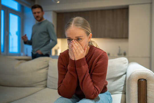 Heartbroken wife sitting on couch in disbelief and sadness in front of angry complaining husband, psychotic jealous man partner accusing woman in infidelity and lies, toxic manipulative behavior.