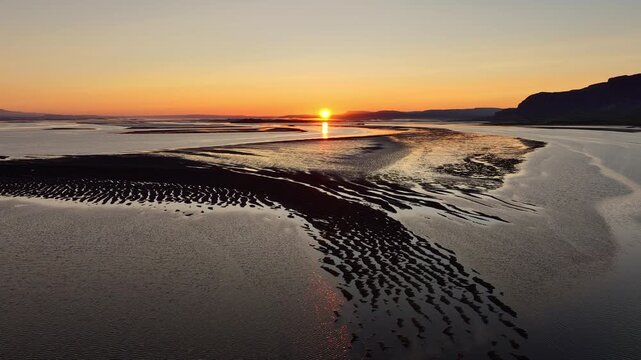 Aerial sunset over tidal flats with winding reflective channels and exposed sandbanks