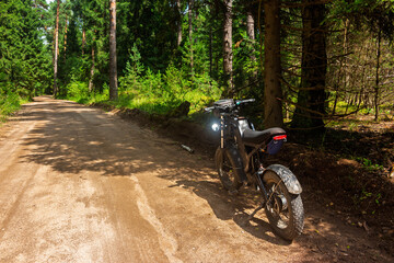 Fototapeta premium Modern electric bike with fat tires parked on a rural dirt road in a sunlit pine forest, adventure travel lifestyle outdoors, summer trail riding scene for active leisure enthusiasts