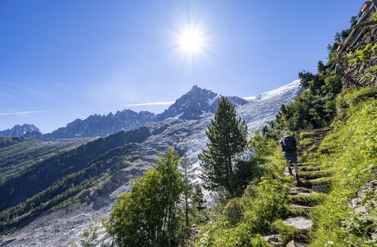 Hiker on hiking trail La Jonction, view of glacier Glacier des Bossons with sun star, behind summit of Aiguille du Midi, Chamonix, Haute-Savoie, France