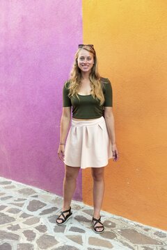 Young woman in dress stands laughing in front of colorful house, orange and pink house facade, Burano Island, Venice, Veneto, Italy