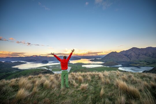 Hiker stretches his arms in the air, panoramic view of Wanaka Lake and mountains at sunset, Rocky Peak, Glendhu Bay, Otago, South Island
