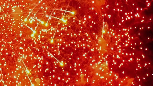 Exploding patterns of fire and light fill the darkness. Trails of sparks fall against a background of vibrant red during an evening celebration in the Park.