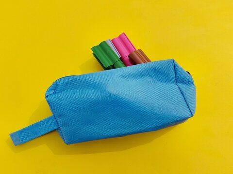 Blue pencil case with colorful markers on yellow background, back to school, concept