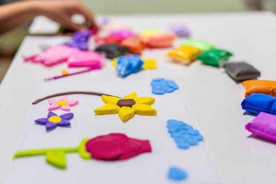 child hands are molding lightweight or colorful modeling clay into various flower shapes on white board or kid people learning art handicrafts and using imagination to create sculpting ideas at school