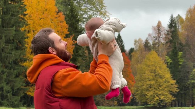 man holding baby playing with stuffed animal in joyful outdoor autumnal forest setting. medium shot side view. family moments, parenting, childhood. orange, red, yellow, green.
