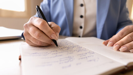 Naklejka premium Closeup businesswoman writing, taking notes with pen in notebook at office desk, organizing thoughts, planning business tasks and creative ideas. Concept of personal development, learning activity