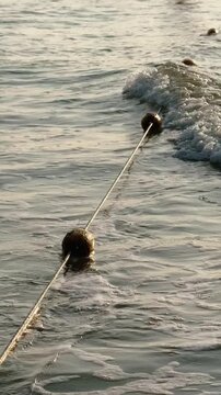 Vertical shot of Beach Safety Buoy stretched on a rope in Foamy Breaking Waves pointing rip current zone at the beach