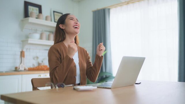 Funny euphoric young asian woman celebrating winning or getting ecommerce shopping offer on computer laptop. Excited happy girl winner looking at notebook celebrating success