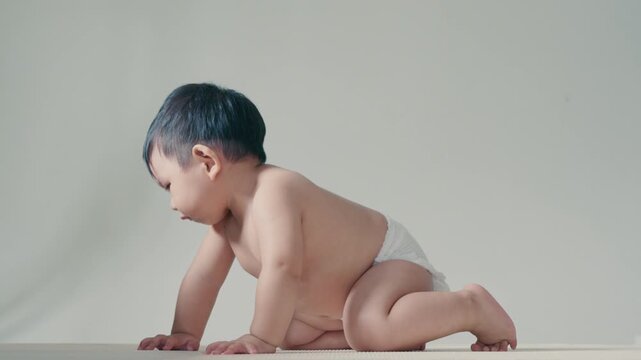 4K Happy adorable infant wearing diaper crawling forward with cheerful smile.