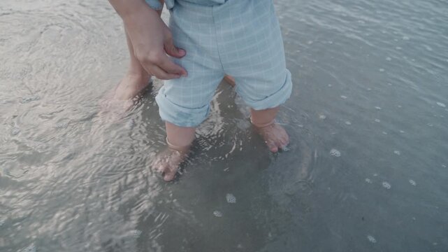 close up of a baby boy's feet standing in shallow sea water on a sandy beach