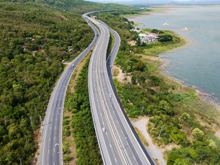 Obraz premium Drone aerial view of Motorway M6 Bang Pa-in–Nakhon Ratchasima expressway running beside Lam Takhong Reservoir in Nakhon Ratchasima, Thailand under cloudy skies