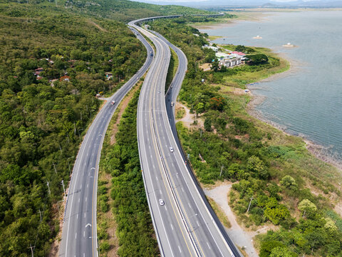 Drone aerial view of Motorway M6 Bang Pa-in&ndash;Nakhon Ratchasima expressway running beside Lam Takhong Reservoir in Nakhon Ratchasima, Thailand under cloudy skies
