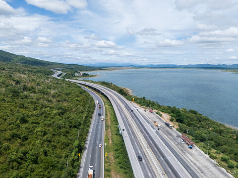Drone aerial view of a highway running beside a reservoir with lush green mountains, Transportation infrastructure and renewable energy concept