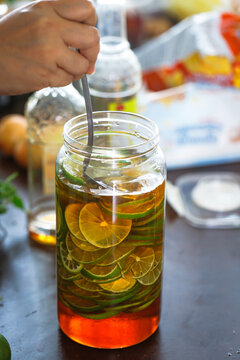 Hand stirring fresh lime slices in a glass jar filled with honey during homemade honey lime infusion preparation. Healthy drink, natural ingredients, and food preservation concept