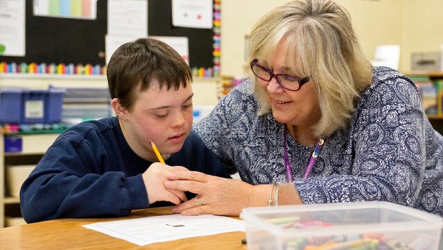 Inclusive Education: Supportive Teacher Helping a Boy with Down Syndrome in Classroom