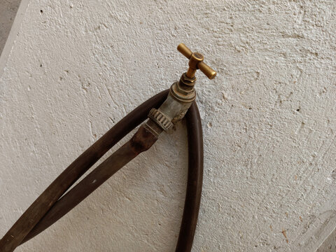 An old brass tap on a white concrete wall connected to a pipe hose with copy space for text. Standing pipe. Fetching water from pipe. World water day.